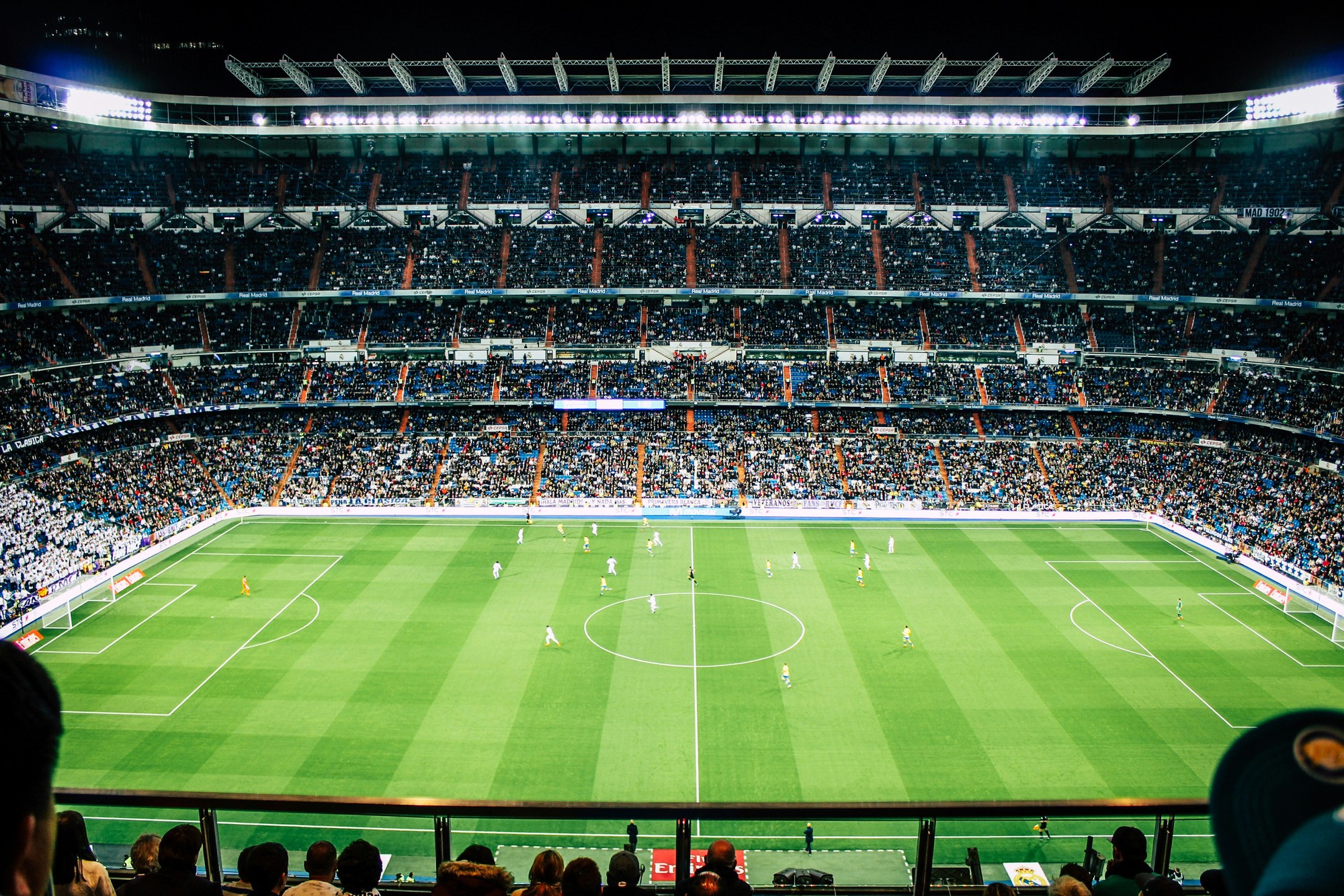Stadion de fotbal luminat noaptea, cu gazonul și tribunele pline de spectatori vizibile